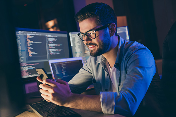 Man in low lit computer room looking at phone