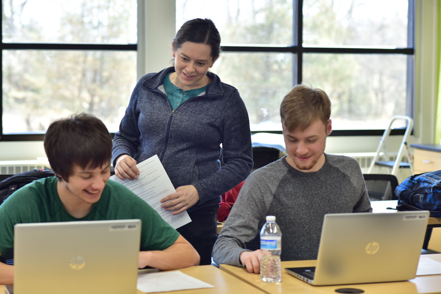 Teacher checking on students working on laptops