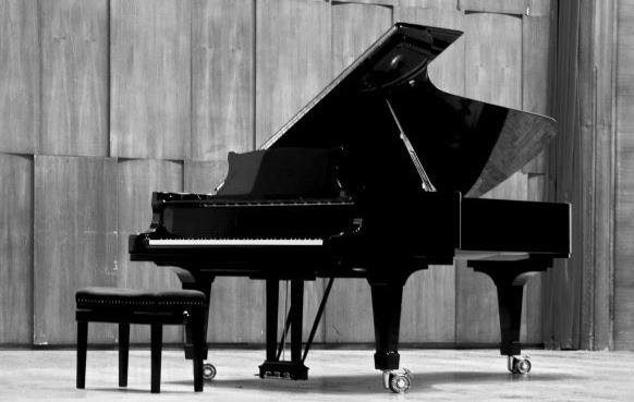 Black and white image of a grand piano on stage in an empty theatre