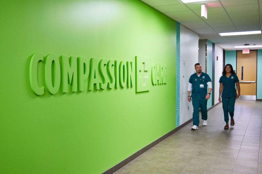 Two nurses walking past compassion and care sign on wall